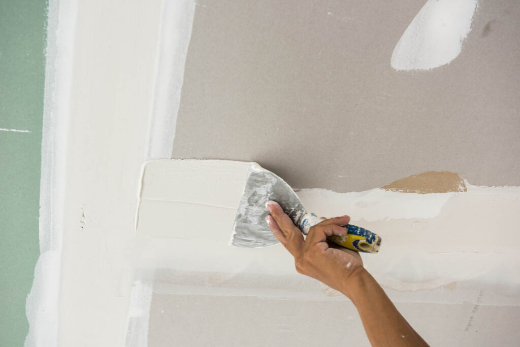 man hand with trowel plastering a ceiling, skim coating plaster walls